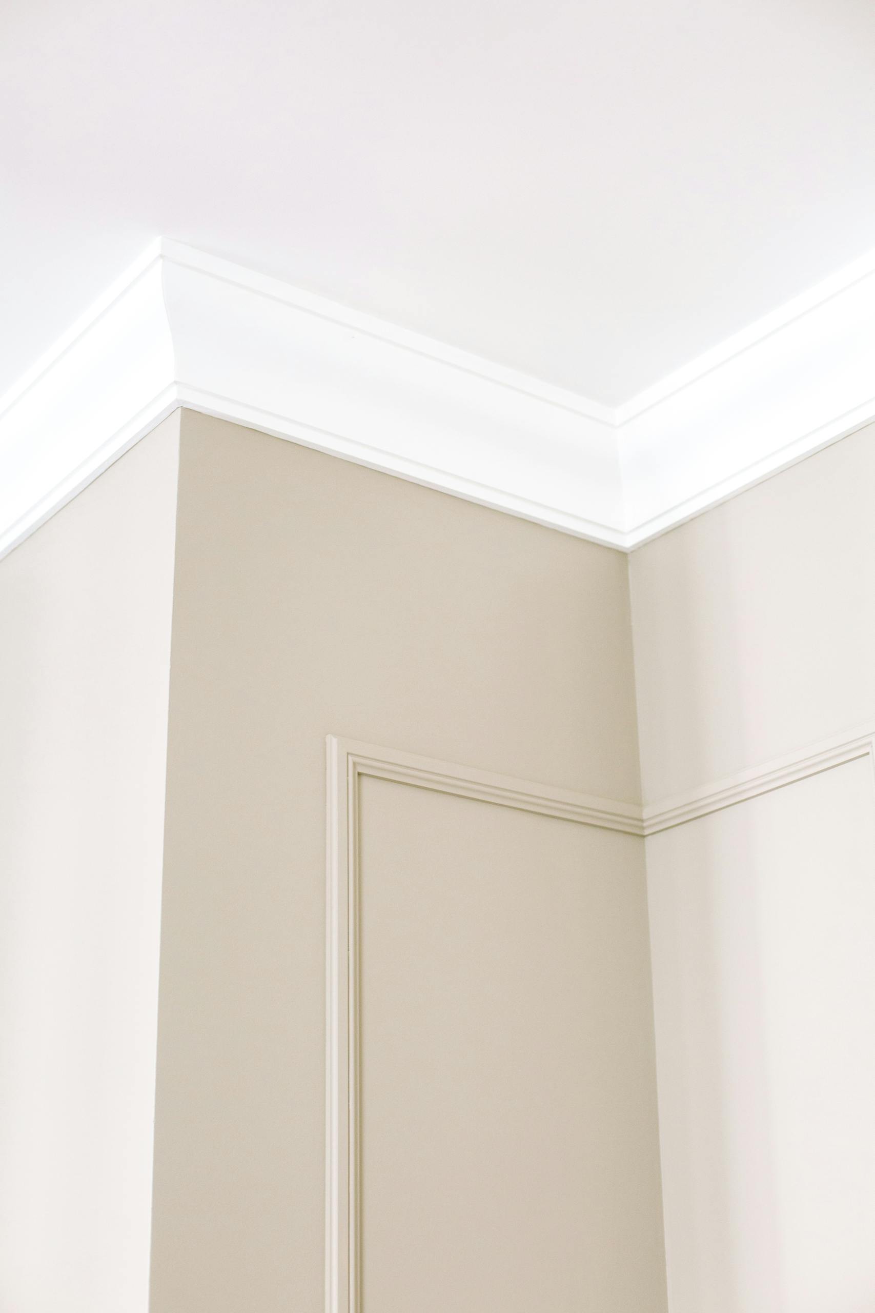 Close-up of intricate ceiling moulding and beige walls with minimalist design, showcasing home renovation details.