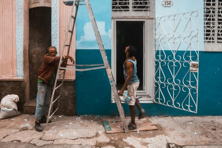 Two men repainting a colorful blue and pink urban building facade in daylight.